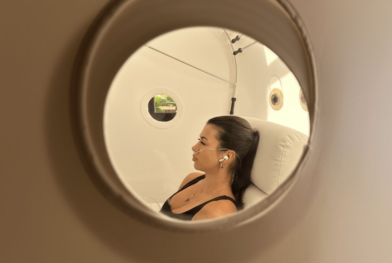 View through the porthole of a hyperbaric oxygen chamber showing a client during an HBOT for brain fog session at SILA Miami, FL.