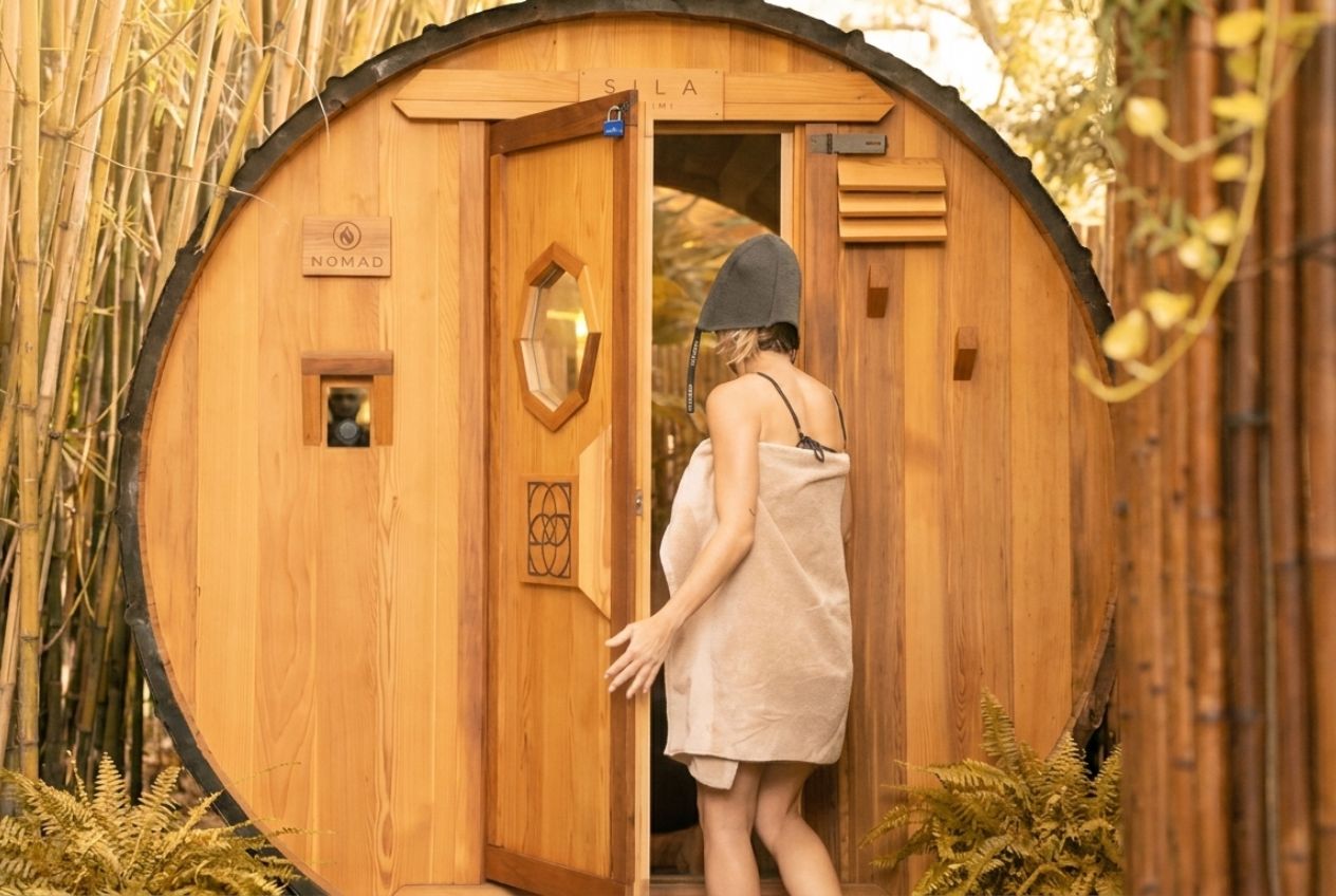 Woman entering the cedar barrel sauna for a sauna for stress relief session at SILA Miami's outdoor sanctuary in Upper Buena Vista, FL